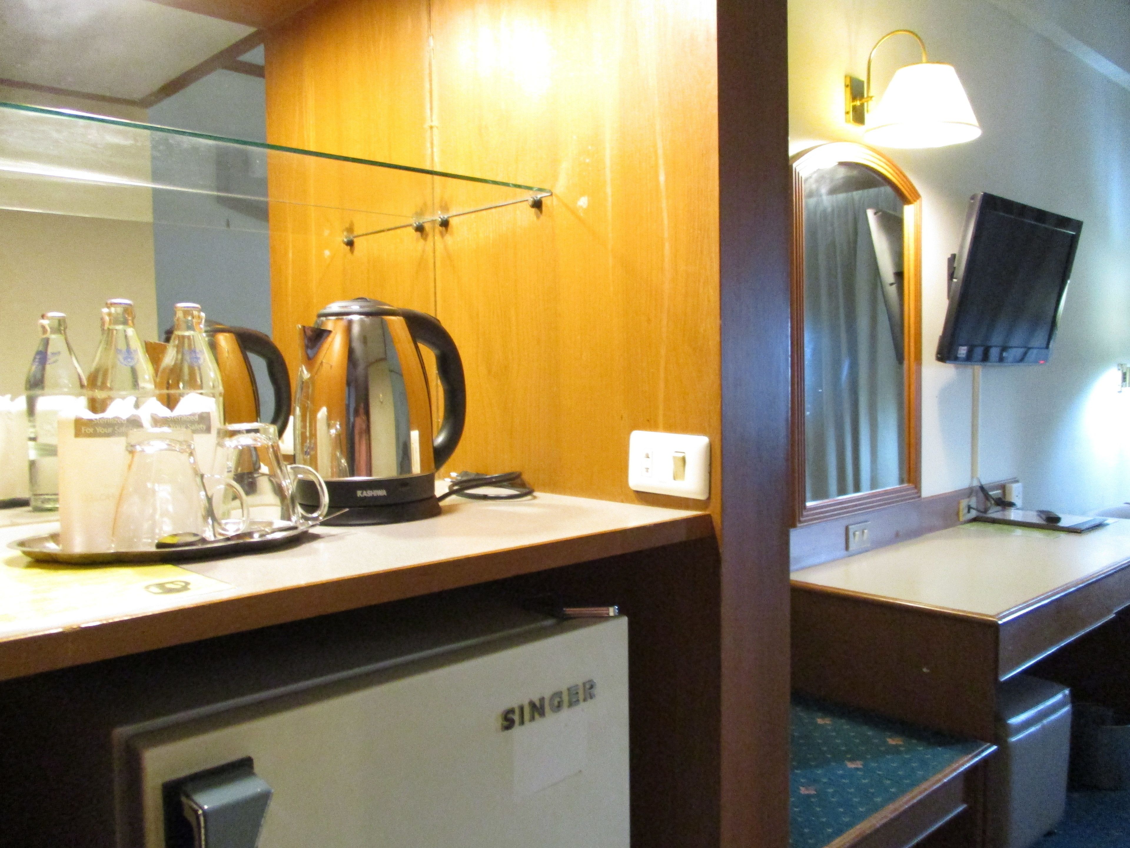 A hotel room with a wooden desk, a kettle, and a refrigerator.