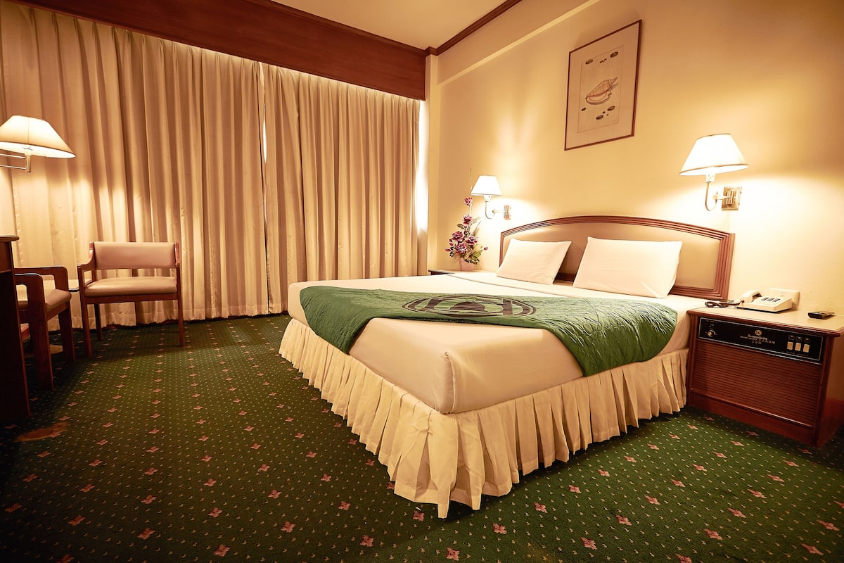 Una habitación de hotel con una cama bien hecha, una silla, una mesita de noche con lámpara y un teléfono instalado en la pared.