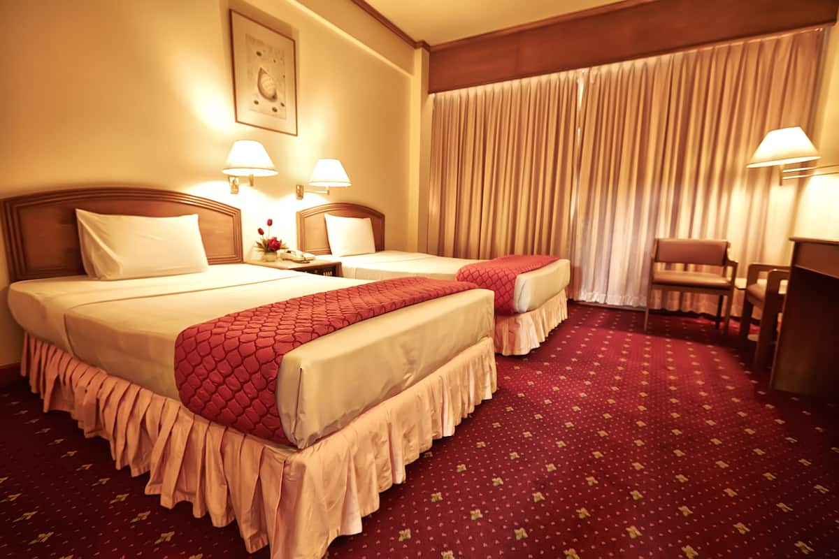 Habitación de hotel con dos camas, un escritorio, una silla y un ventanal con cortinas.