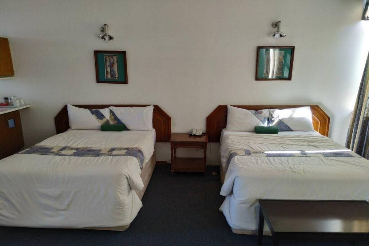 A hotel room with two single beds, a small wooden nightstand, and a desk.