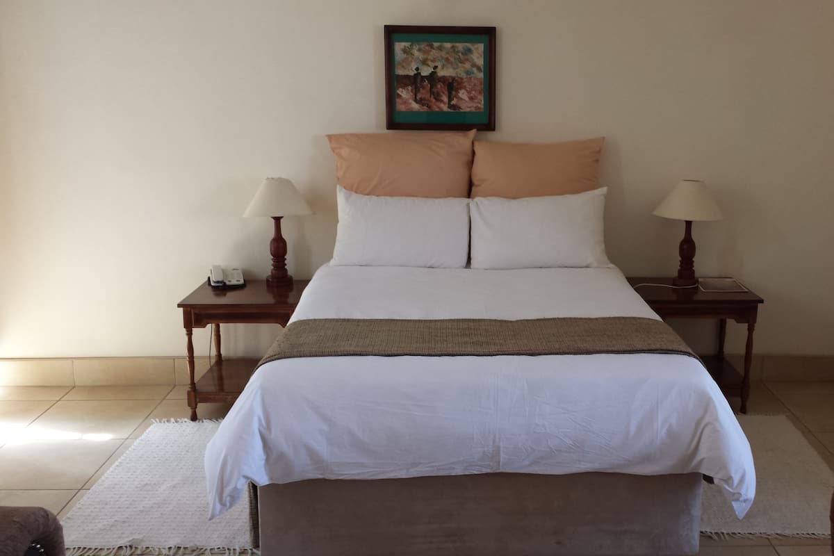 A neatly arranged hotel room with a bed, two bedside tables, a lamp on each table, a painting on the wall, and a small chair.