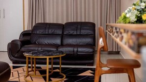 A living room with a dark leather sofa, a round coffee table, and a wooden chair. - Bulawayo Central Lodge (Bulawayo)