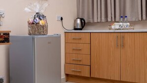 A compact kitchenette with a refrigerator, wooden cabinets, a kettle, and a basket of groceries. - Bulawayo Central Lodge (Bulawayo)