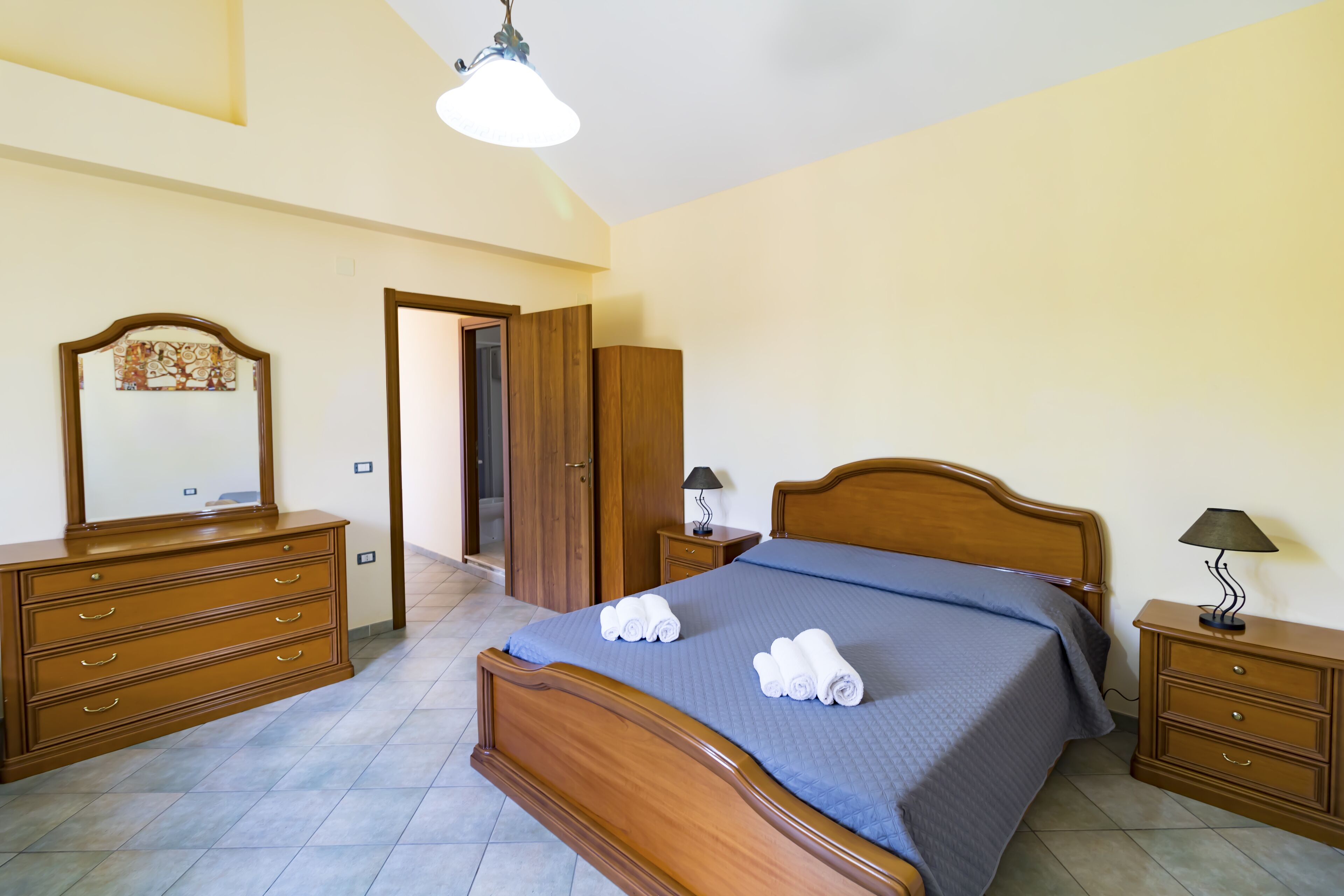 Ein Schlafzimmer mit einem hölzernen Bett, einem Schminktisch, einem Nachttisch und einem Spiegel.