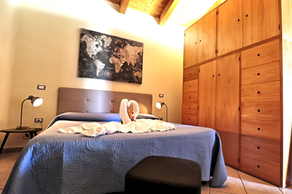 Un dormitorio con una cama grande, un armario de madera, un mapa del mundo en la pared y dos lámparas de noche.