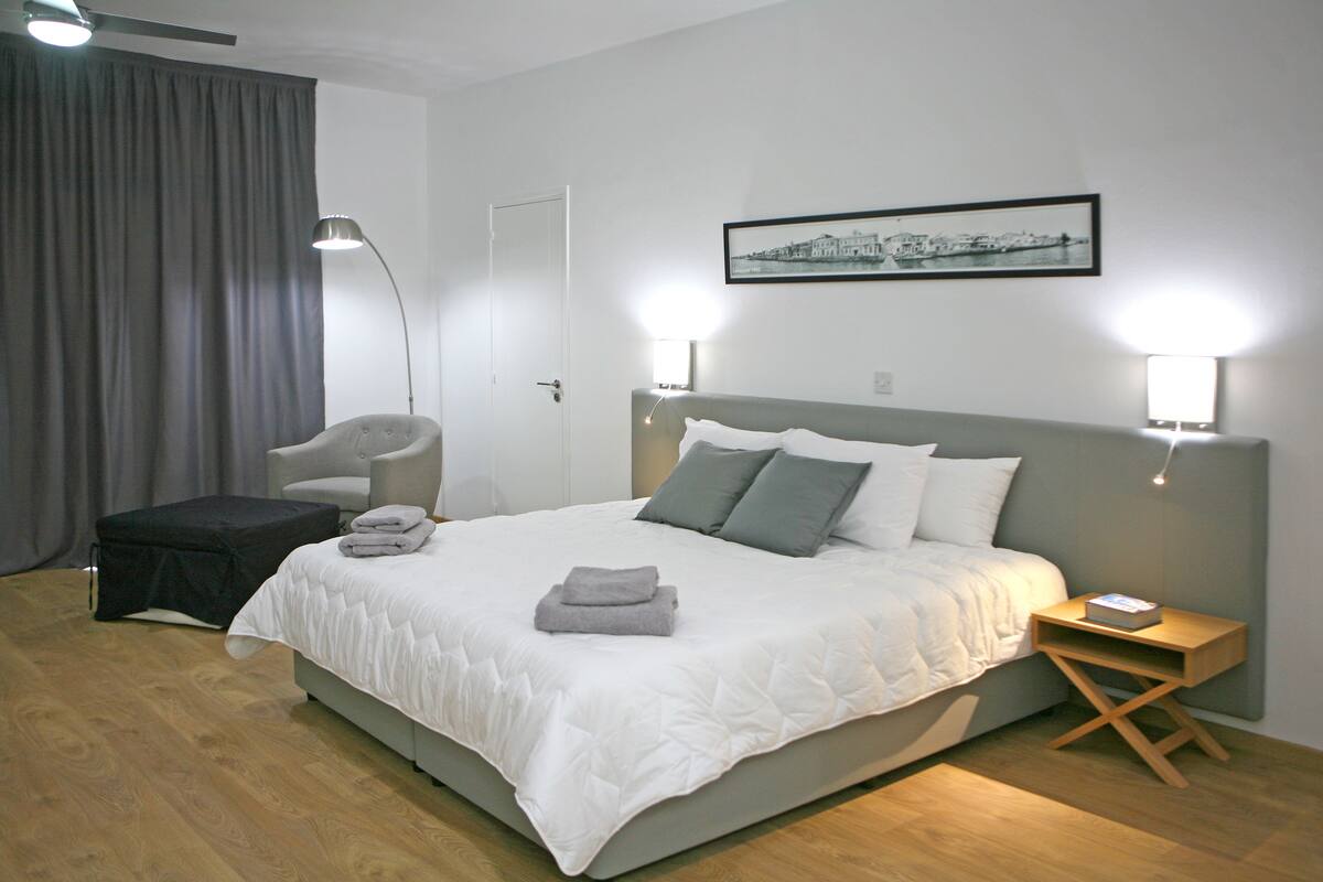 A modern bedroom with a large bed, a chair, a bedside table, and a framed picture on the wall.