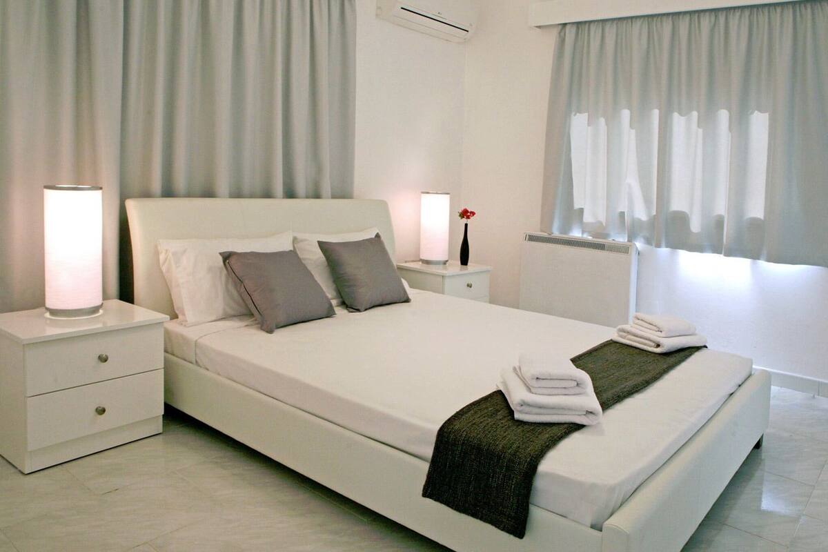 A neatly made bed with pillows, a bedside lamp, and a folded towel on a white nightstand.