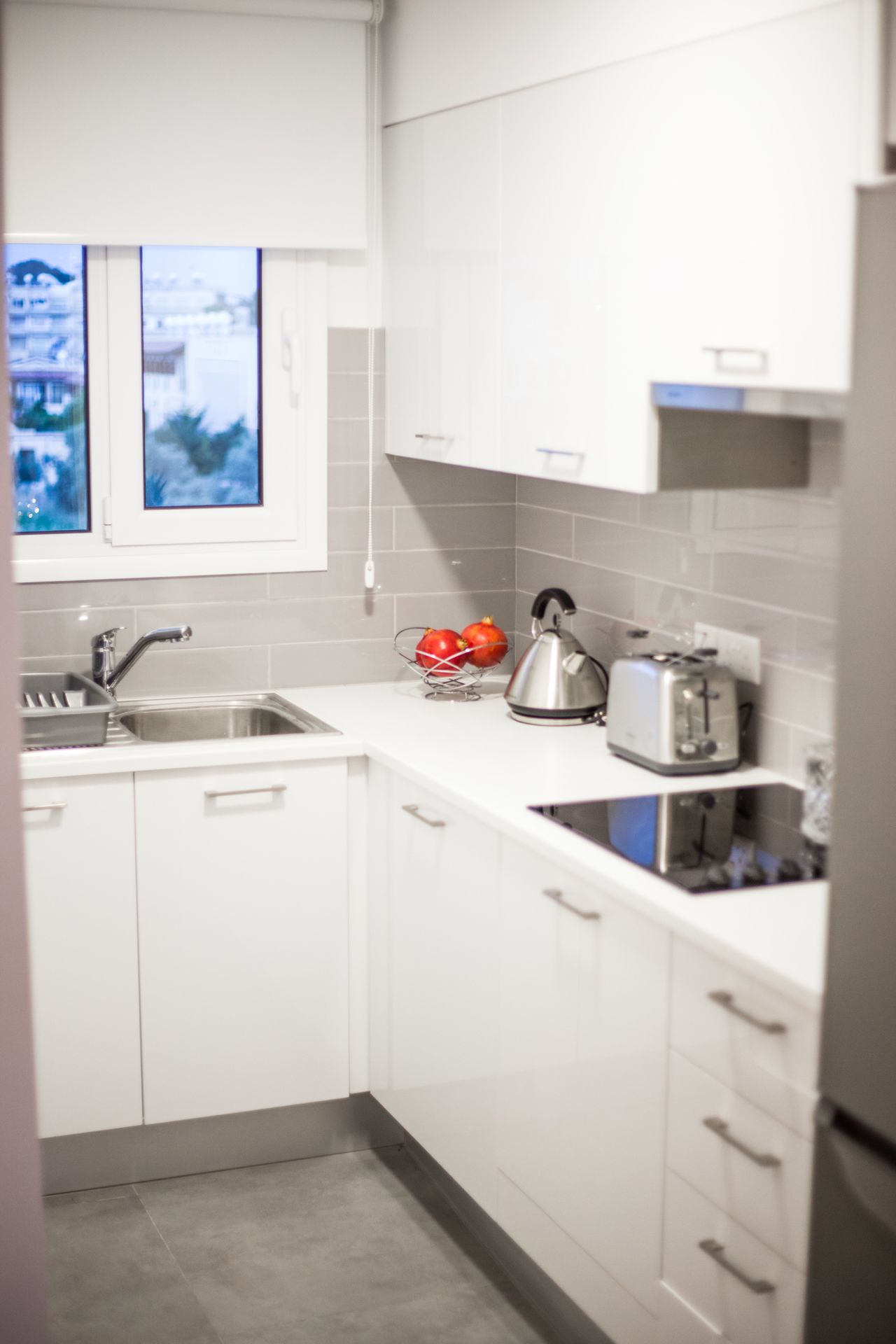 A modern kitchen with white cabinets, a stainless steel sink, a kettle, and a toaster.