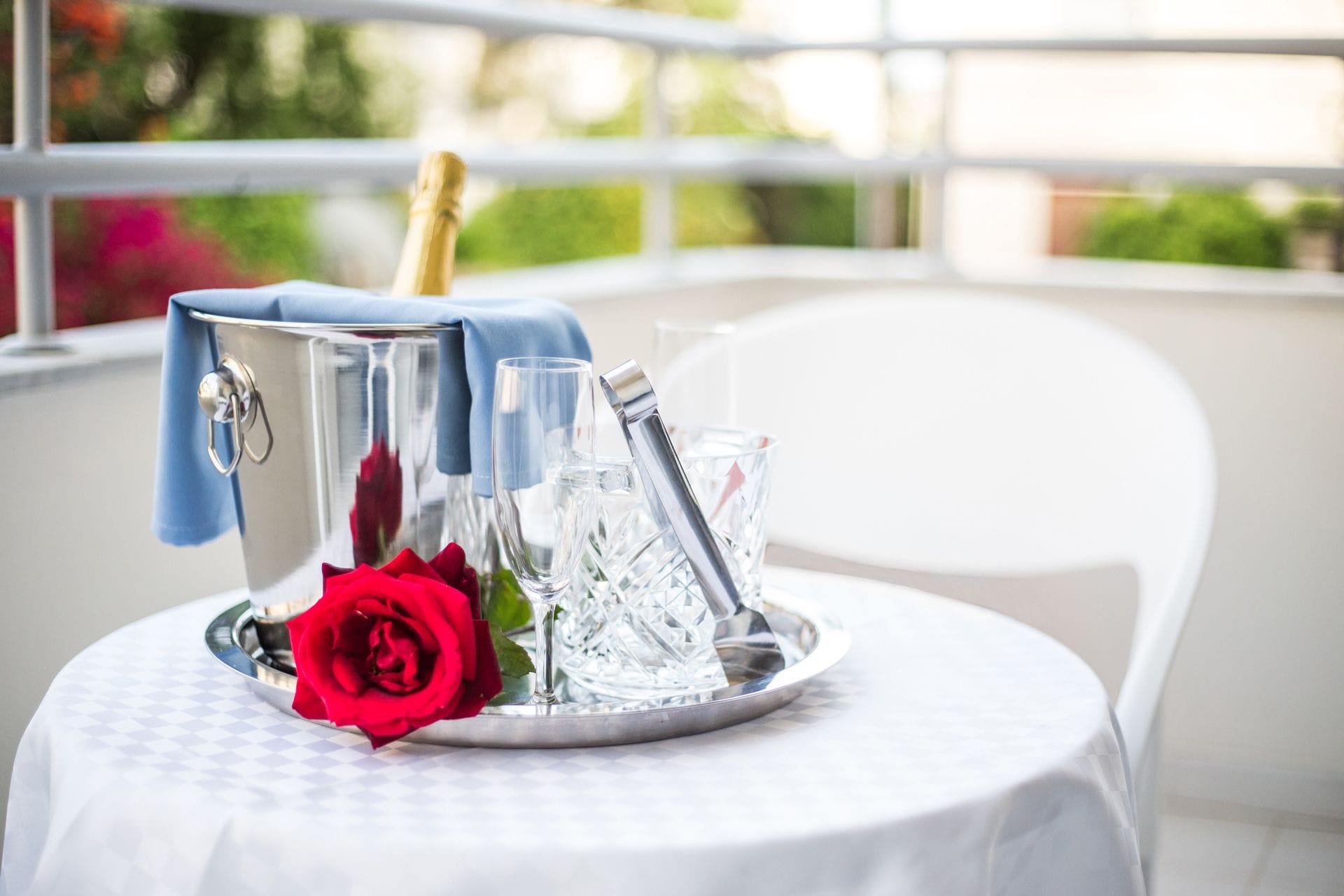 Una mesa con una bandeja de plata que sostiene una botella de champán, copas y una rosa roja.