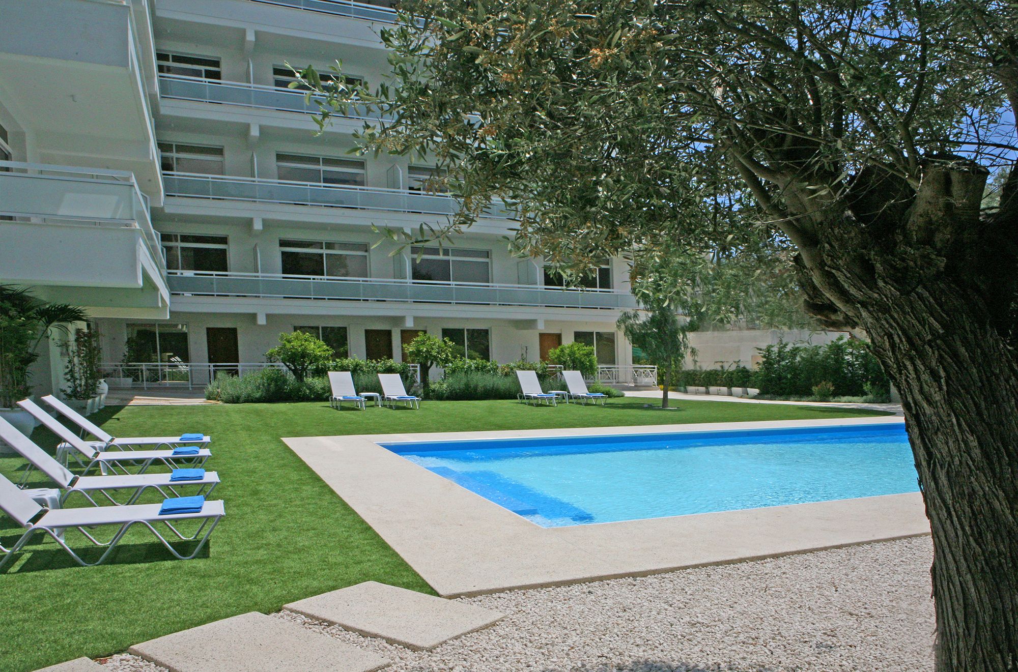 A hotel with a swimming pool, multiple lounge chairs, and a well-maintained lawn.