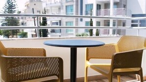 Un balcón con una mesa redonda y dos sillas de mimbre, con vistas a un moderno conjunto de edificios.