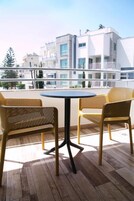 A balcony with a round table and two wicker chairs, overlooking a modern building complex.