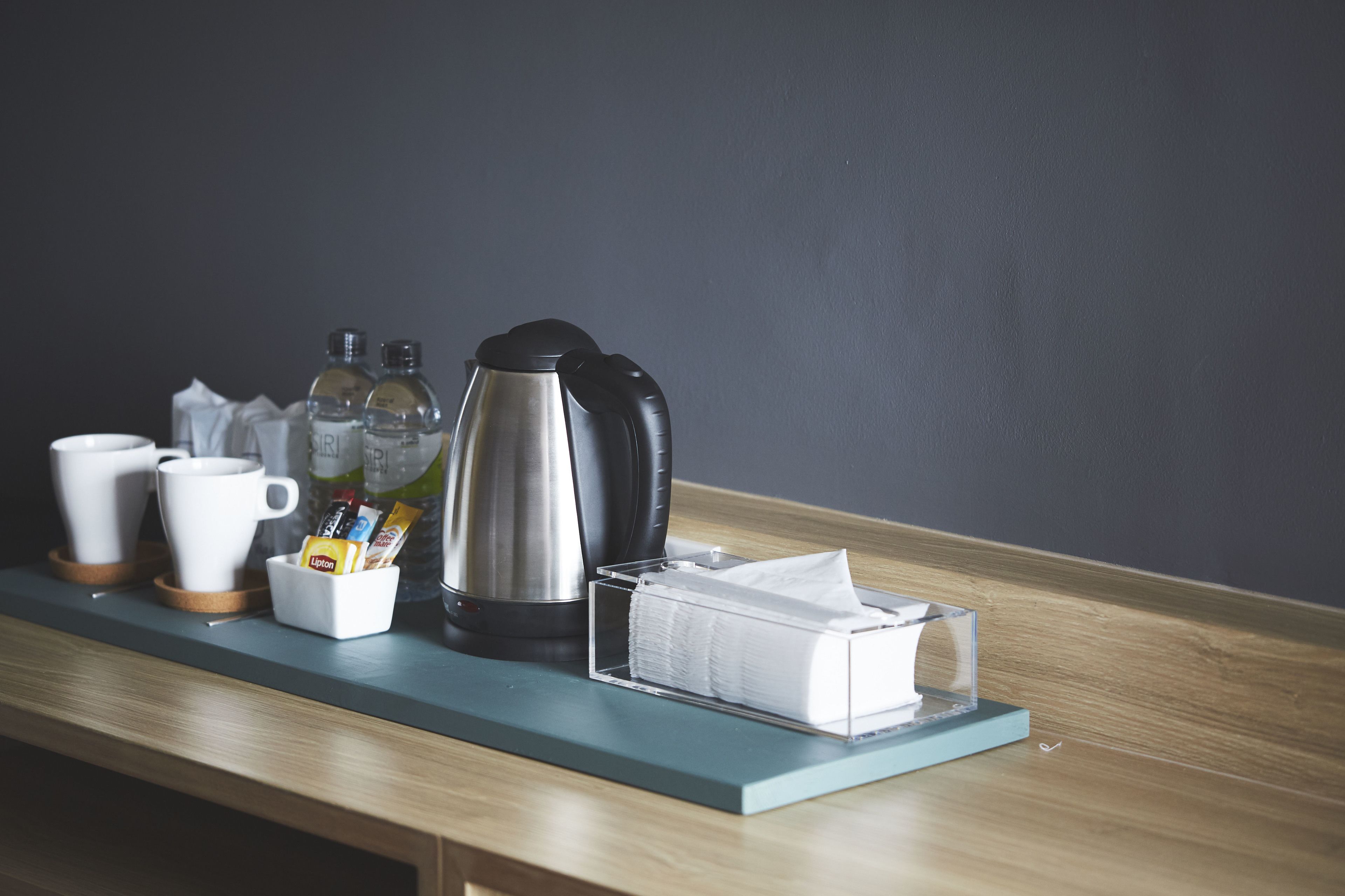 A kitchenette with a coffee maker, cups, and a bottle of water on a wooden counter.