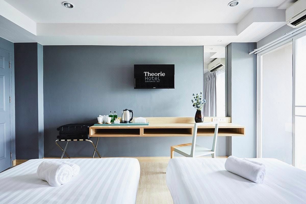 Une chambre d’hôtel avec deux lits, un bureau avec un ordinateur portable, une télévision et une fenêtre avec des rideaux.