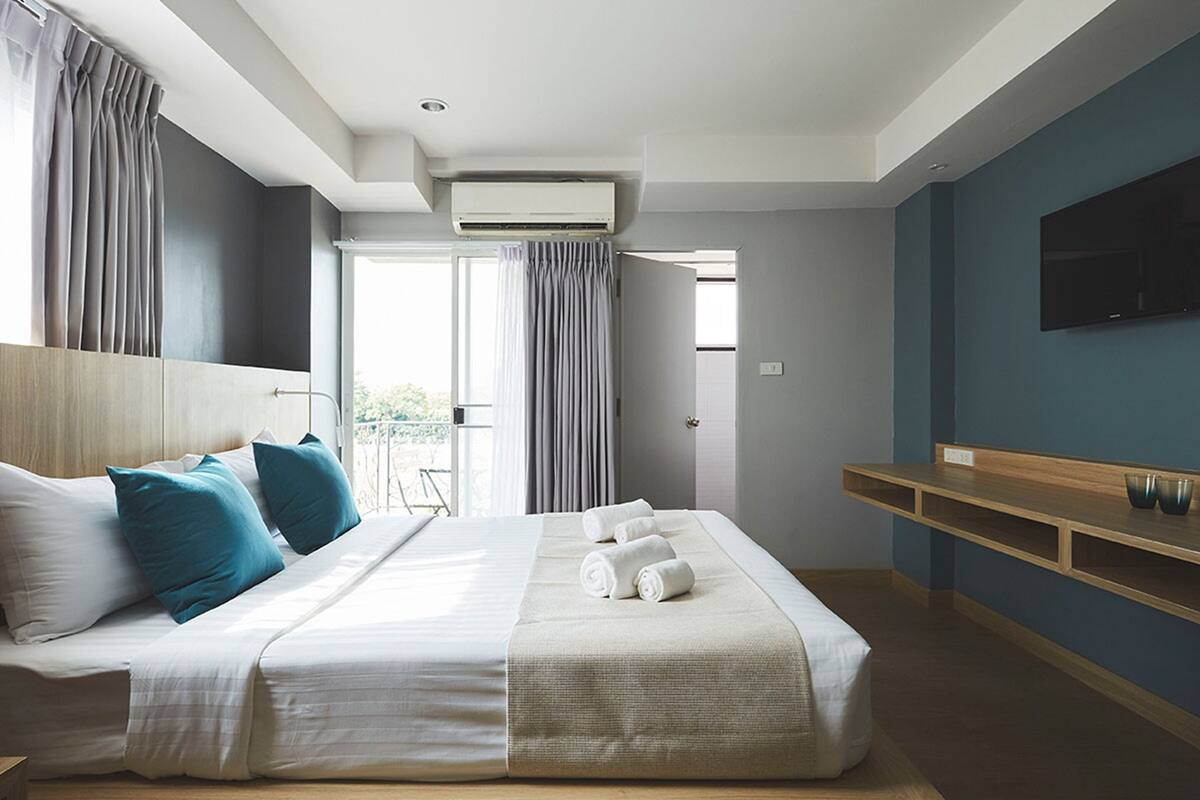 Une chambre d’hôtel avec un lit, une télévision, un balcon et une étagère en bois.