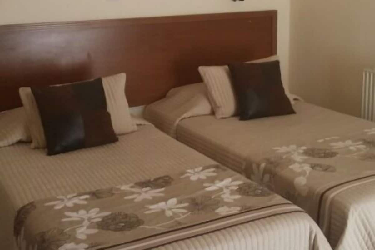 Hotellihuone, jossa on kaksi sänkyä, merimaiseman kuvaava taulu ja kattotuuletin.