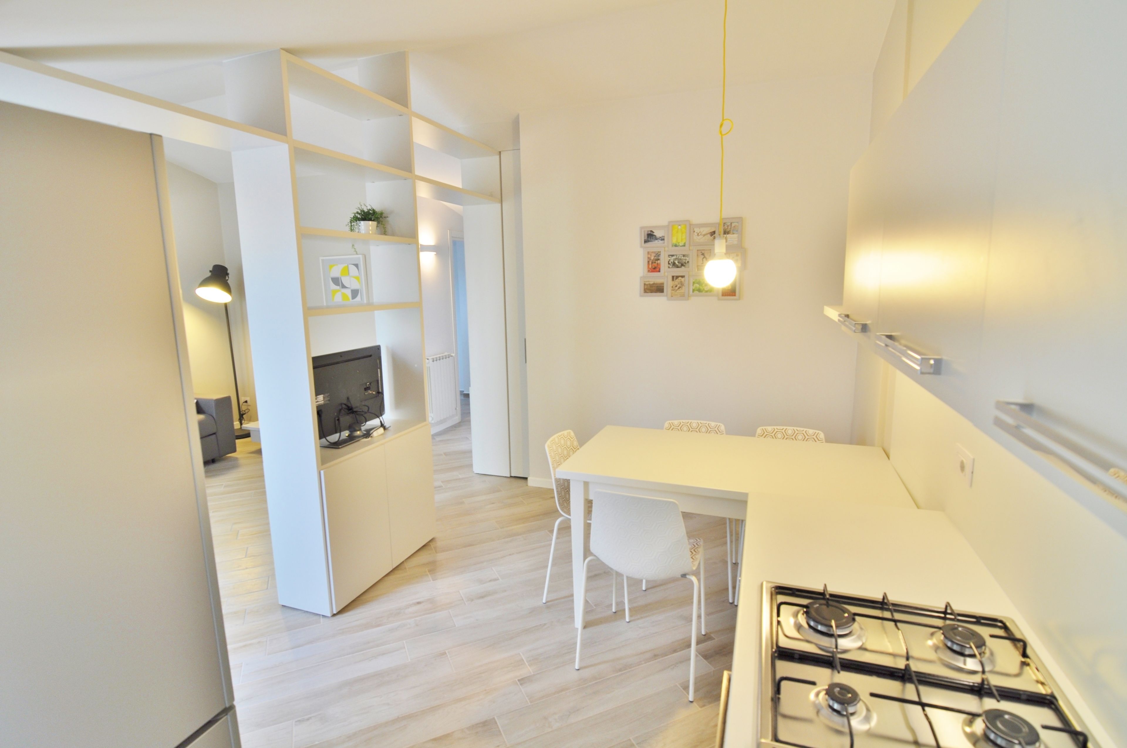 A modern kitchen with white cabinetry, a gas stove, and a dining area with white chairs.