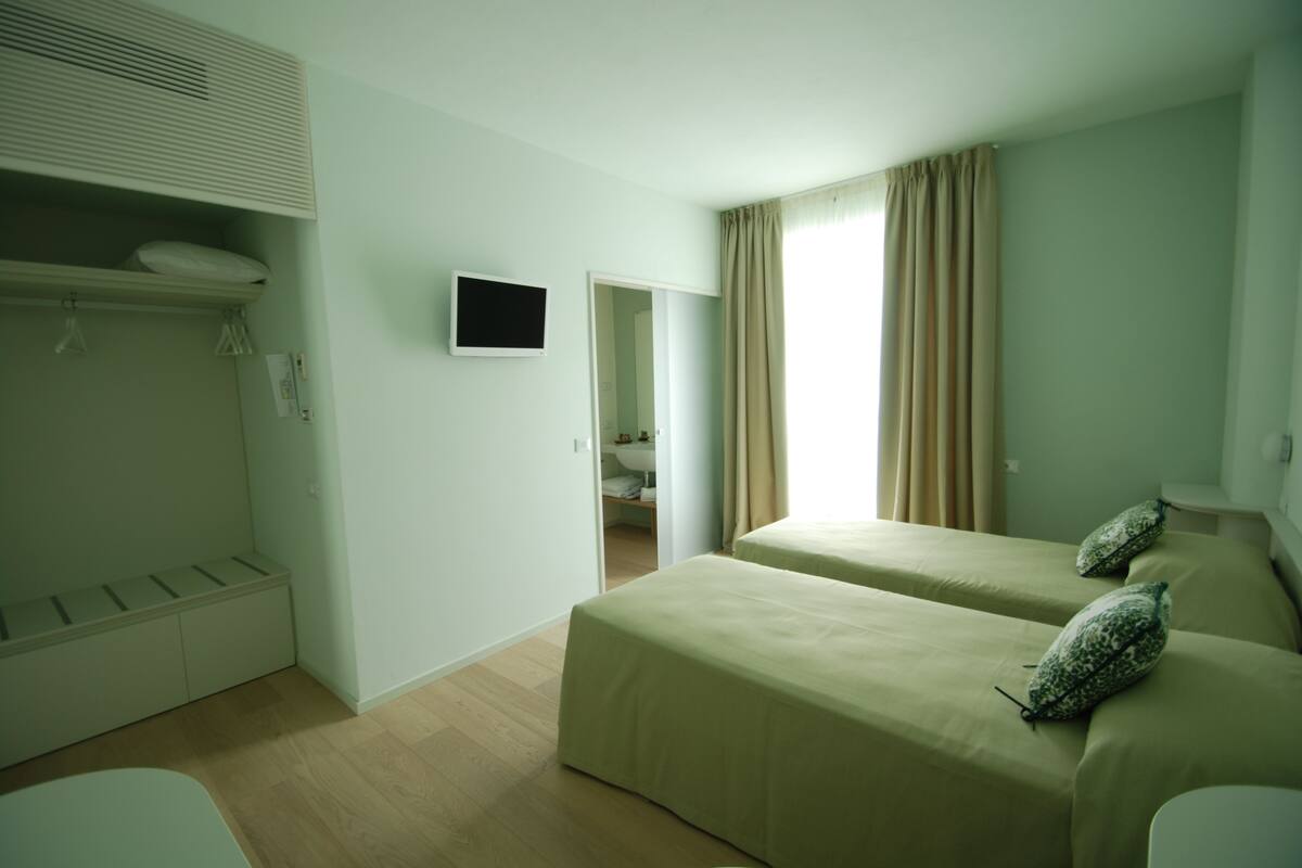 A hotel room with two beds, a TV, a wardrobe, and a bathroom visible through an open door.