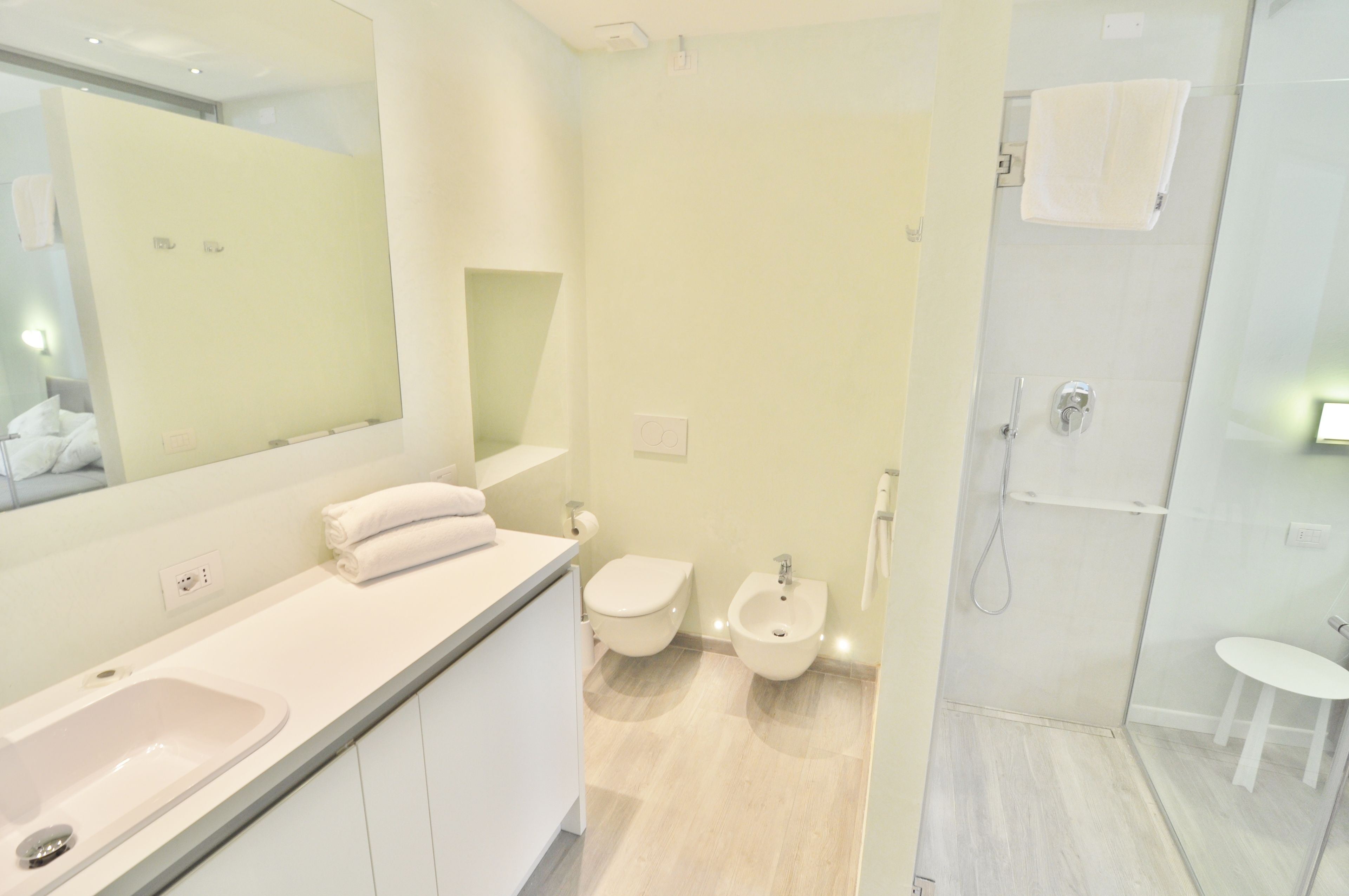 A modern bathroom with a large mirror, a sink, a toilet, a bidet, and a shower area.