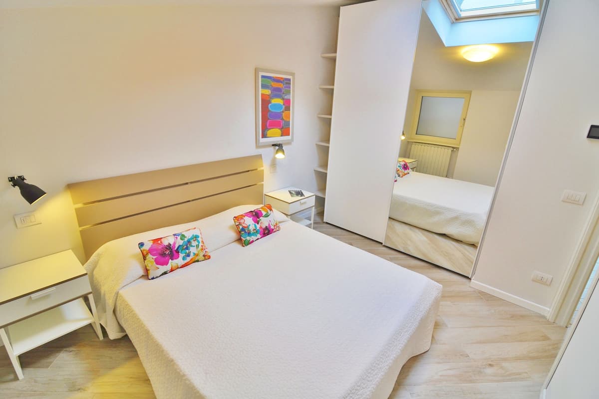 A neatly arranged bedroom with a bed, bedside table, lamp, and a mirror.