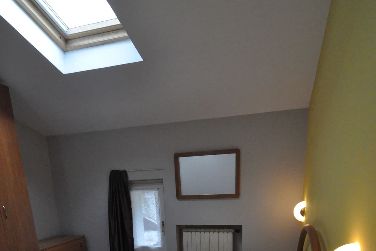 A bedroom with a skylight, a bed, a dresser, a nightstand, and a wall-mounted light fixture.