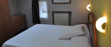 A bedroom with a skylight, a bed, a dresser, a nightstand, and a wall-mounted light fixture.