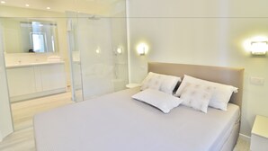 Un dormitorio moderno con una cama grande, cabina de ducha de vidrio y baño con tocador y espejo.