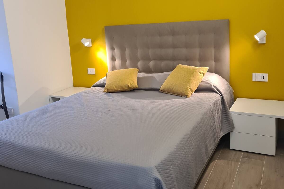 A modern bedroom with a grey bed, yellow walls, and a tufted headboard.