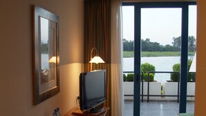 Quarto de hotel com escrivaninha, televisão e vista para a água através de uma porta de vidro.