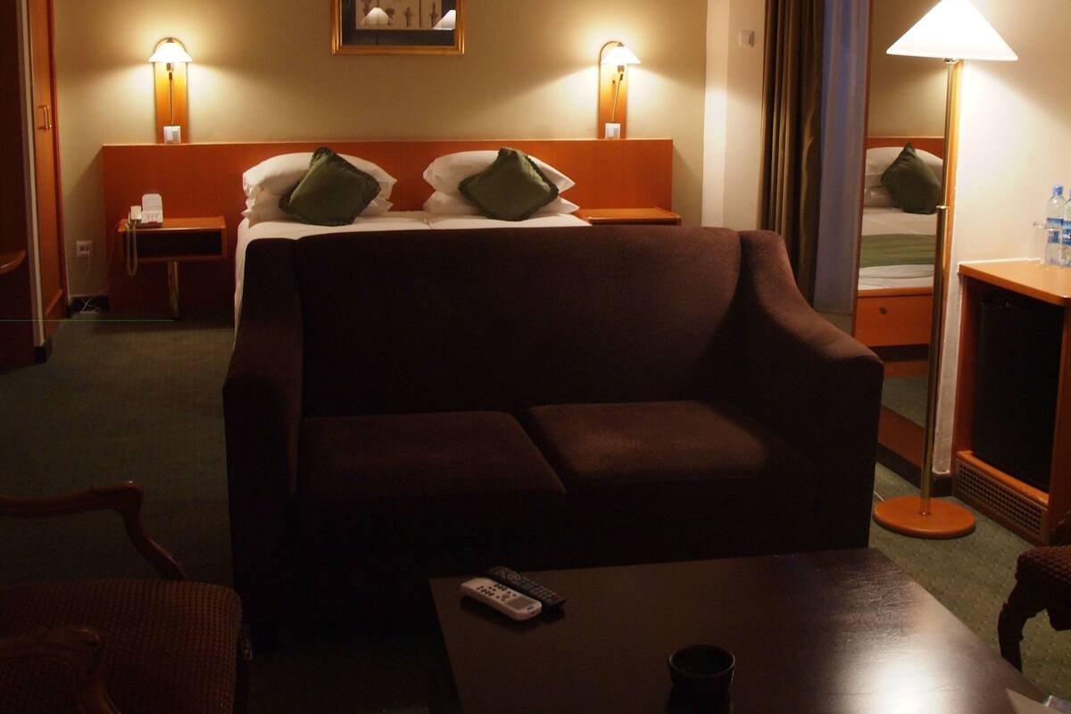 Ein Hotelzimmer mit einer Couch, einem kleinen Tisch, einem Nachttisch, einer Lampe und einem Bett mit Kissen.