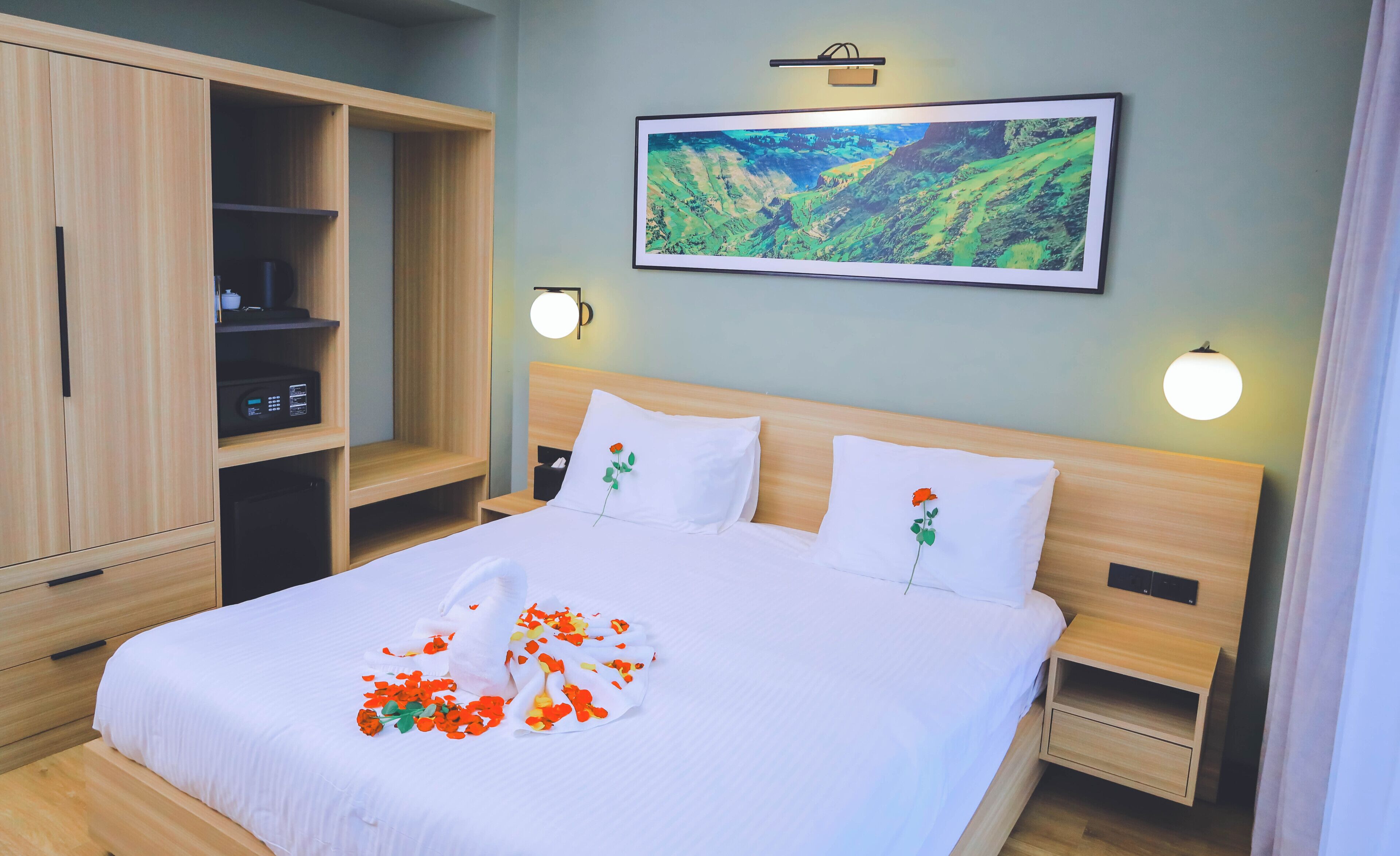 A hotel room with a bed, a wardrobe, a bedside table, and a wall-mounted picture.