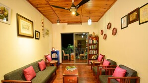 A cozy living room with a wooden ceiling, green sofas with pink cushions, a coffee table, and a bookshelf. - Mistletoe Munnar (Devikolam)
