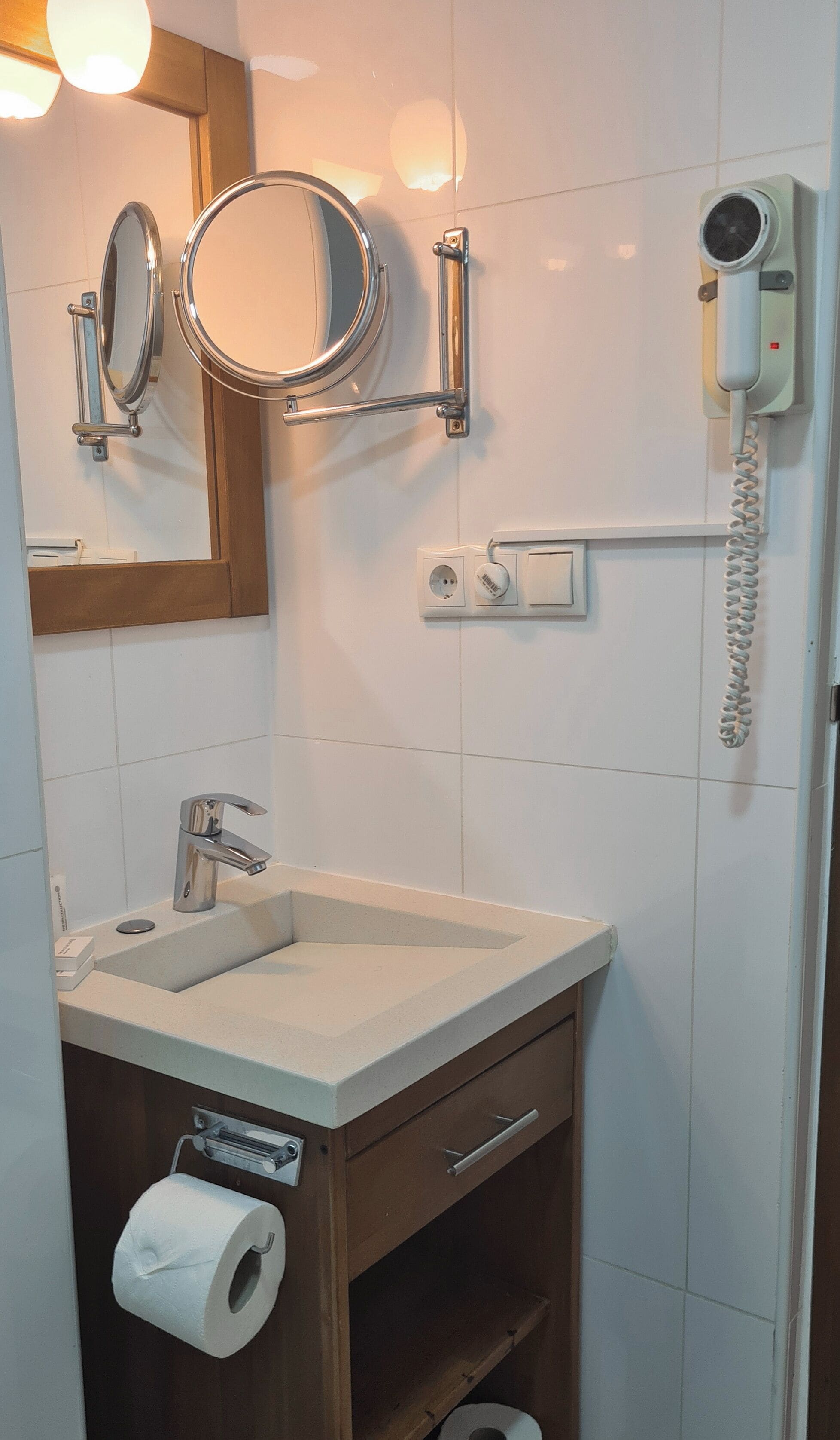 Un bagno con lavandino, specchio, carta igienica e asciugacapelli montato a parete.