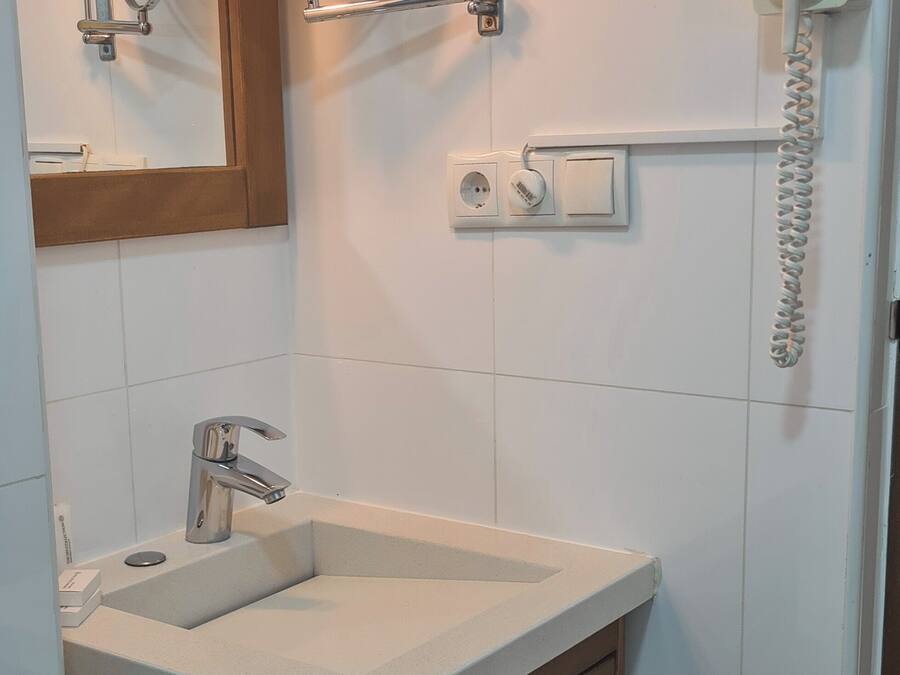 Un baño con lavabo, espejo, papel higiénico y un secador de pelo fijado a la pared.
