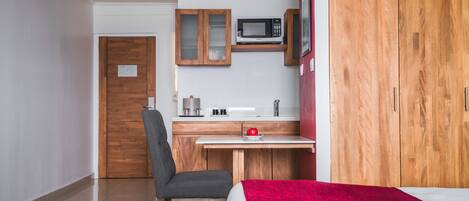 Habitación de hotel compacta con armario de madera, kitchenette con microondas, un escritorio pequeño y una silla.
