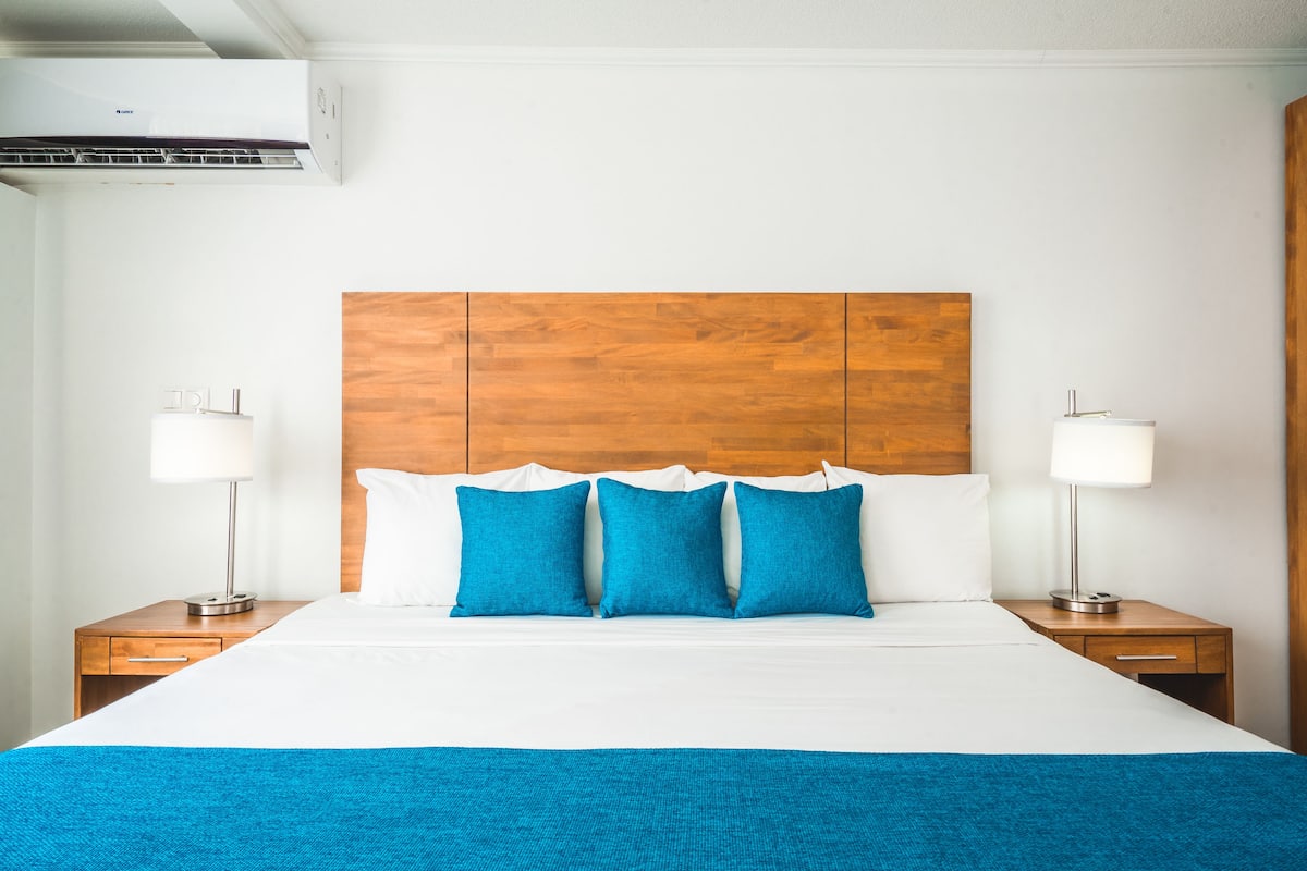Una habitación de hotel con cabecera de madera, ropa de cama blanca y dos lámparas de noche.