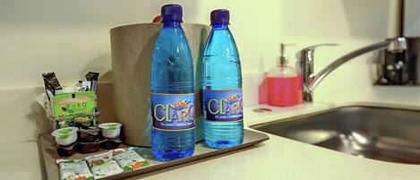 Una encimera de cocina con dos botellas azules de agua marcadas 'CLARO', un dispensador de jabón y una bandeja con alimentos y paquetes.