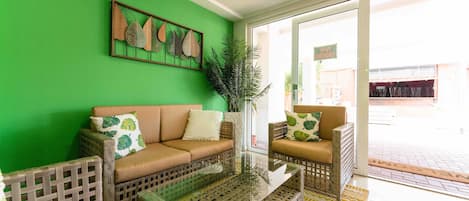 A room with a green wall, a glass coffee table, wicker furniture, and a potted plant.
