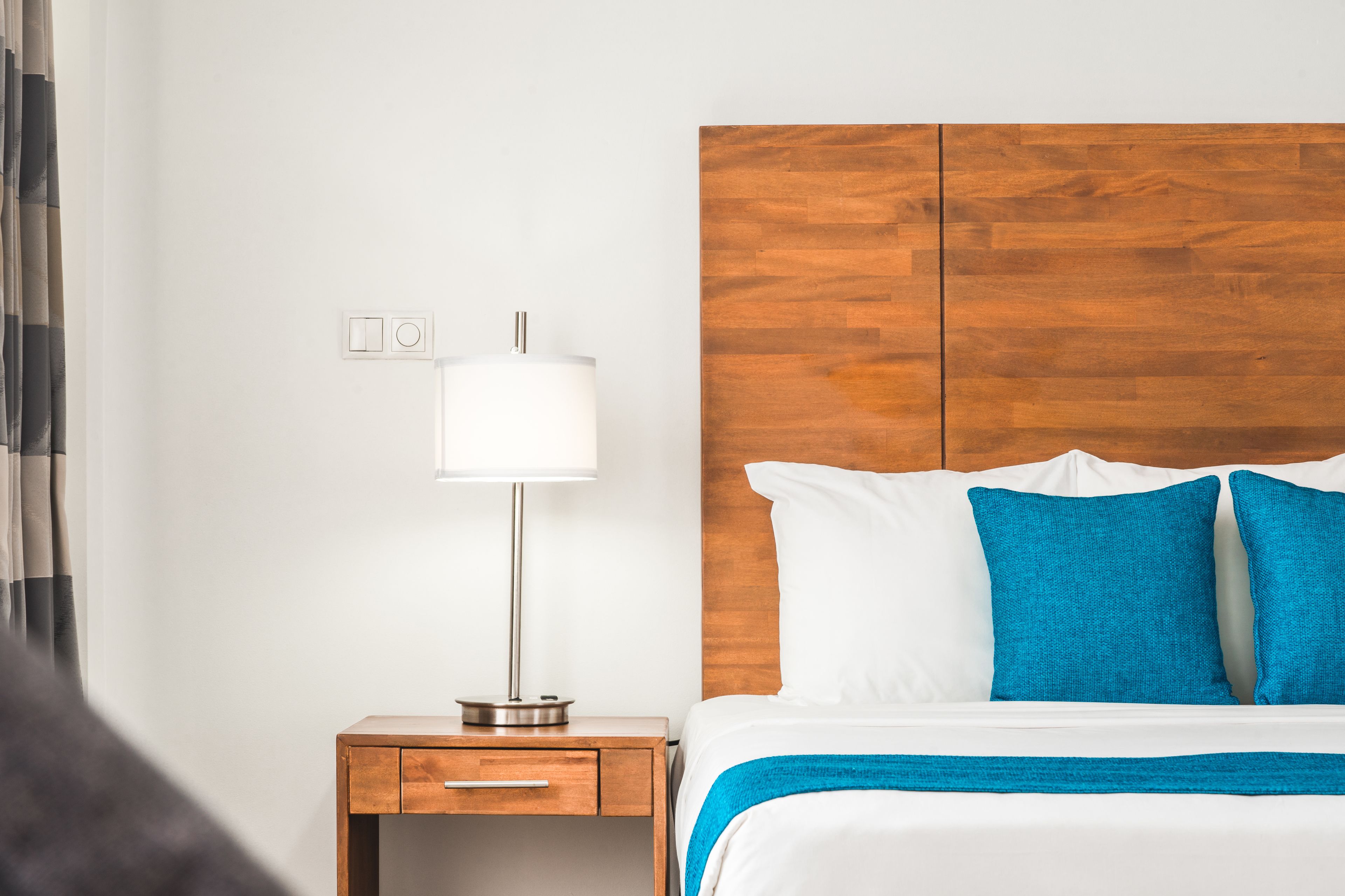 Una habitación de hotel con cabecera de madera, una mesita de noche con lámpara y una cama con ropa de cama blanca y azul.