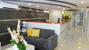 A hotel reception area with a sofa, a water dispenser, and a flower arrangement. - Majestic City Suites & Beach Hotel (Willemstad)