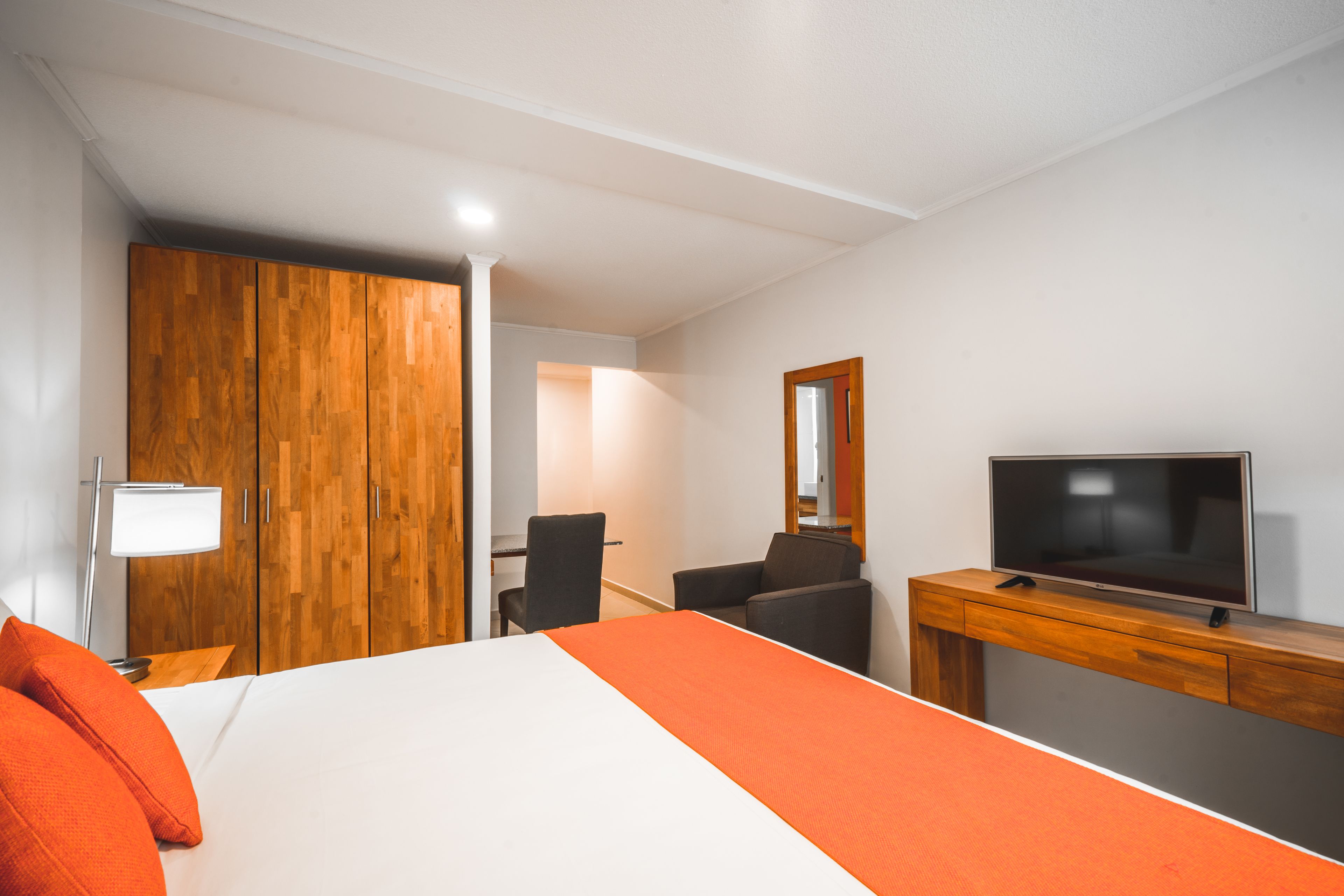 Una habitación de hotel con cama, escritorio con televisor, una silla y armario.