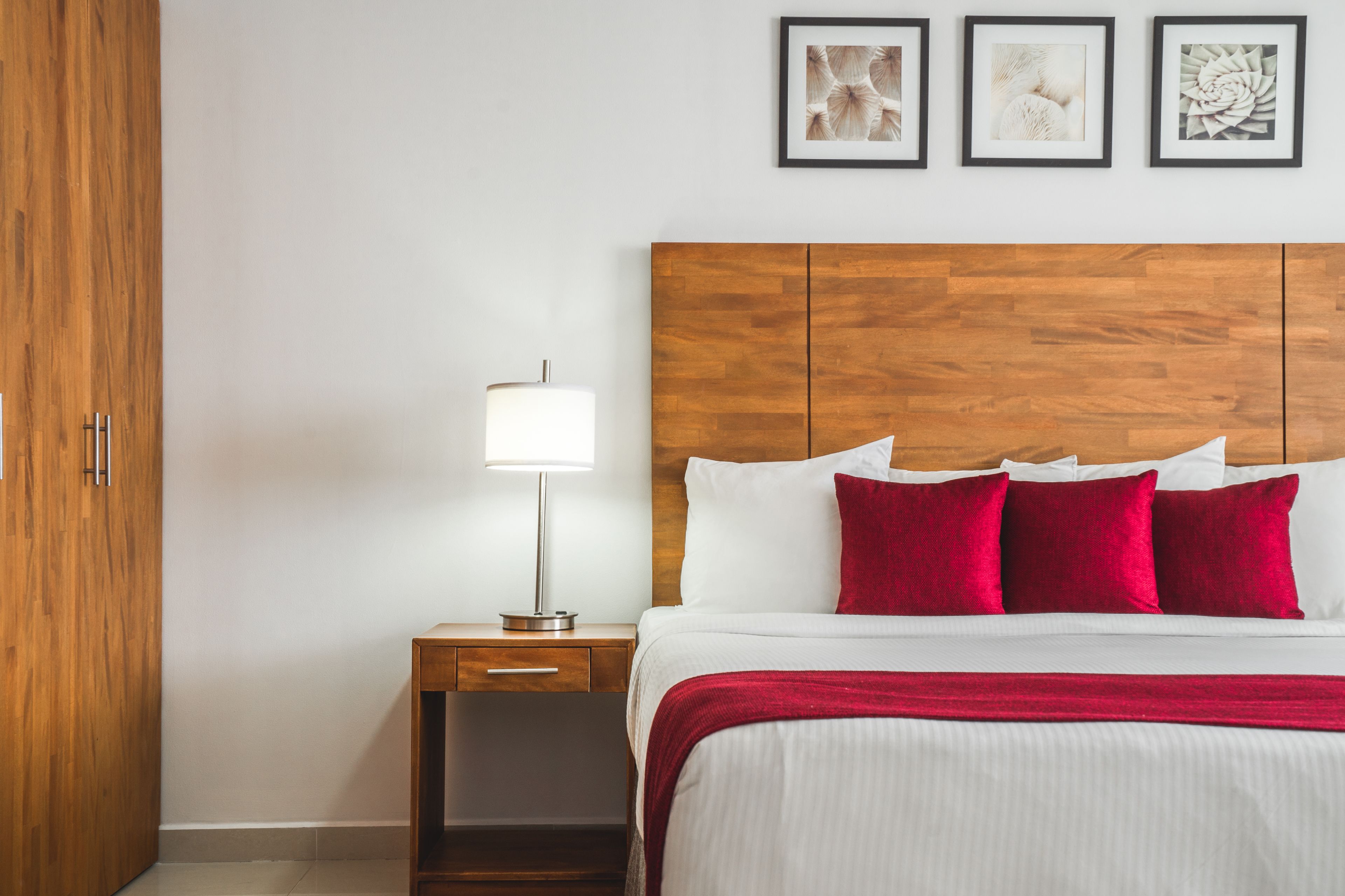 A hotel room with a wooden headboard, a bedside table with a lamp, and three framed pictures on the wall.