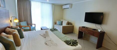 Quarto de hotel com uma cama grande, uma escrivaninha, uma televisão e uma janela com cortinas.