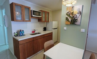 Una cocina compacta con armarios de madera, un microondas, un refrigerador, un lavamanos y una mesa de comedor.
