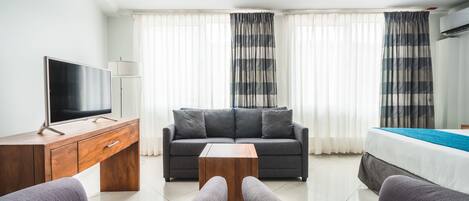 A modern hotel room with a flat-screen TV, a sofa, a coffee table, and a bed.