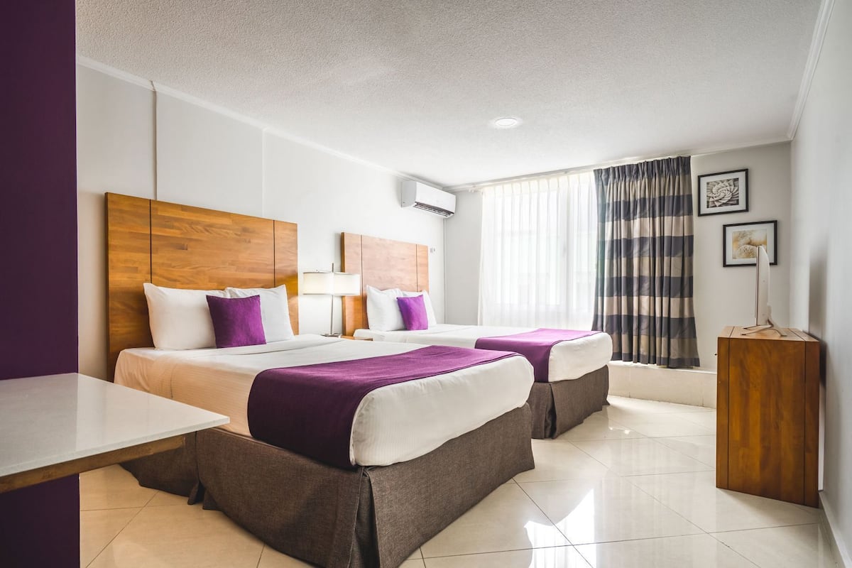 Habitación de hotel con dos camas, un escritorio, un armario de madera y una ventana con cortinas.