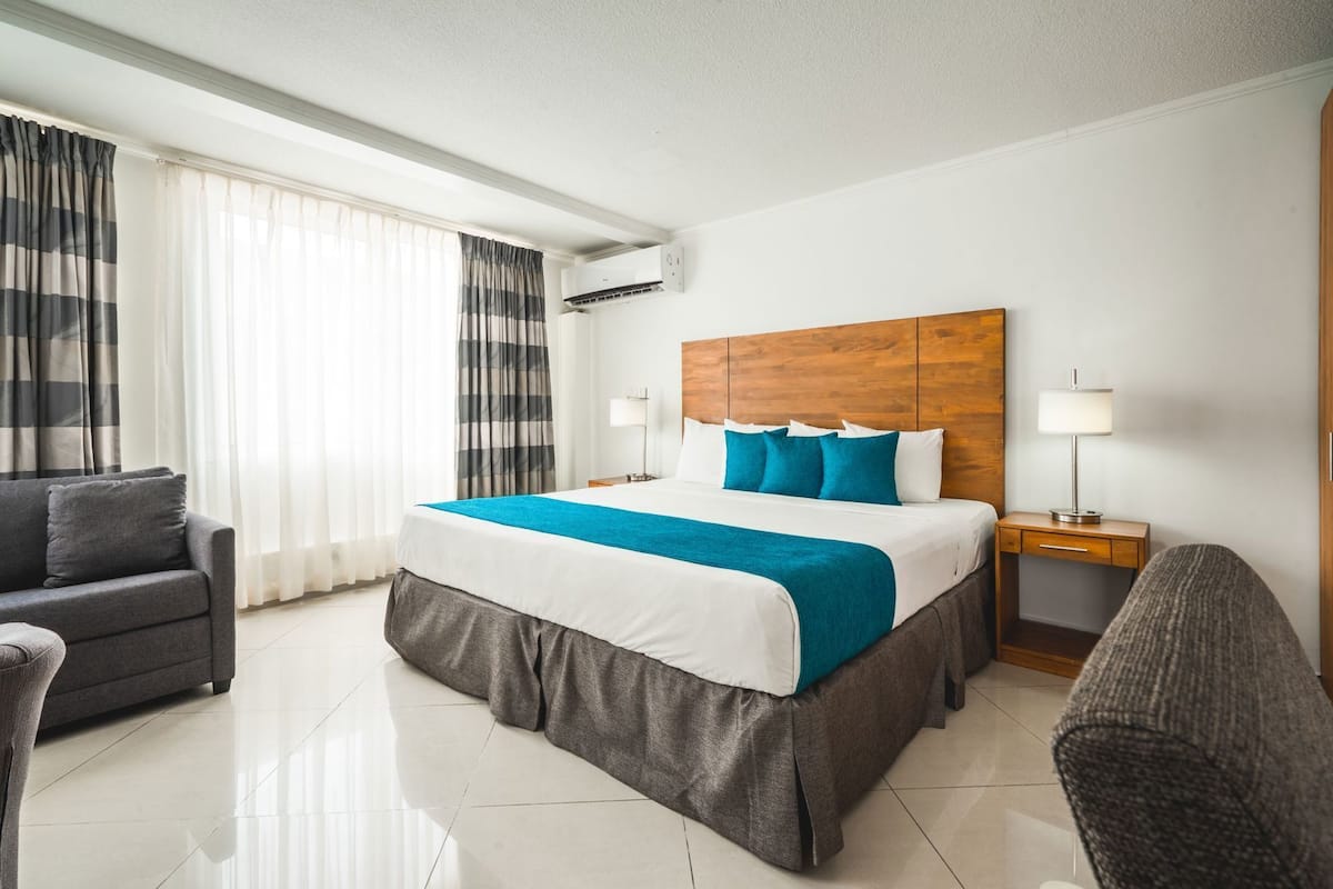 A hotel room with a large bed, a sofa, a desk, and a lamp.