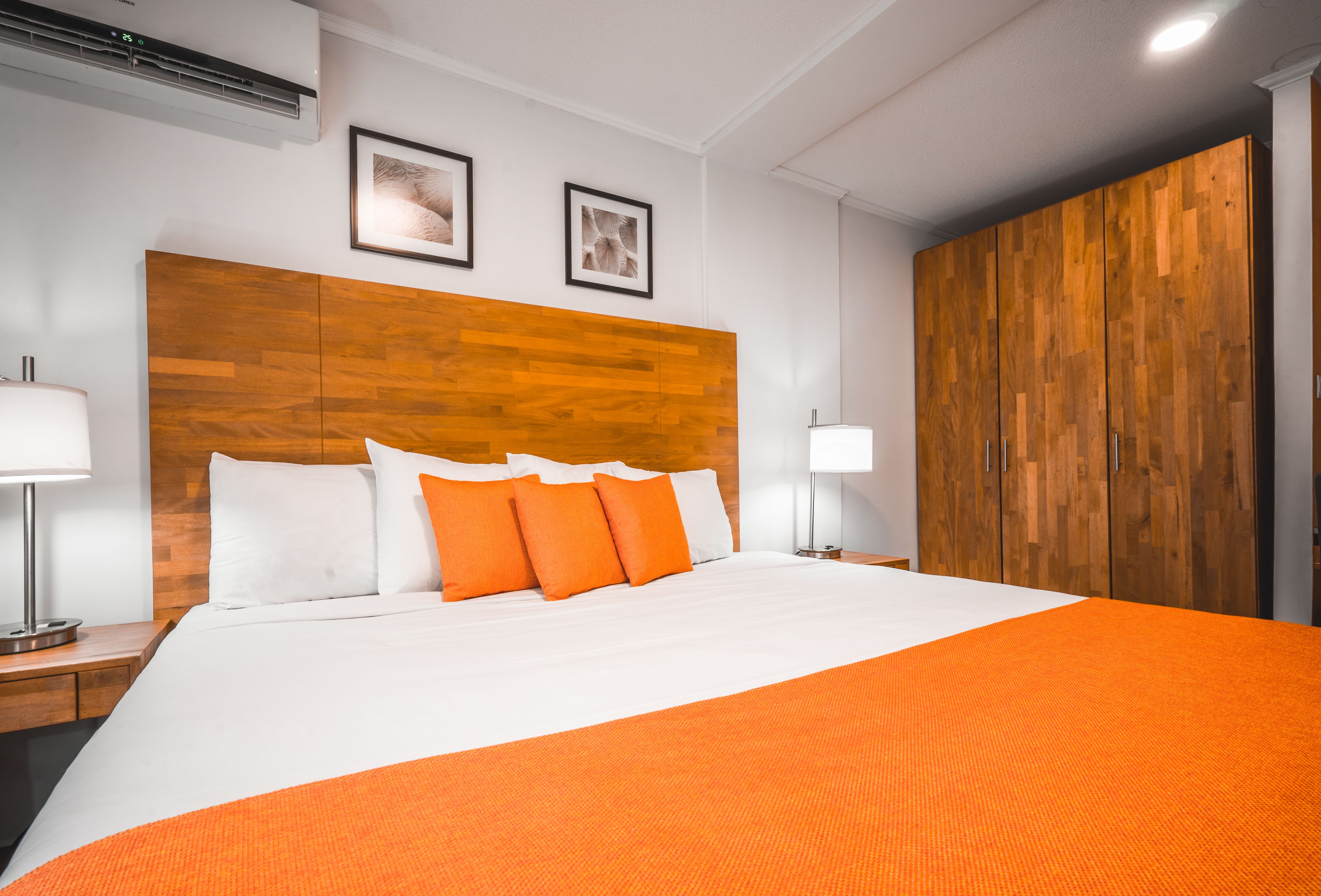 Hotelkamer met groot bed, houten hoofdbord, twee ingelijste foto's aan de muur en een kledingkast.