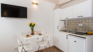 A compact kitchen with white cabinets, a built-in oven, a sink, and a flat-screen TV mounted on the wall. - Apartments Bottega (Dubrovnik)