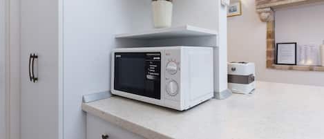 Eine Küche mit einer Mikrowelle auf der Arbeitsfläche, einem Toaster und einer Vase mit Blumen auf einem Regal.
